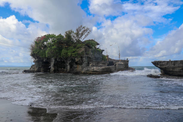 fale rozbijają się na klifie, na szczycie którego znajduje się hinduska świątynia tanah lot. świątynia zbudowana na skale w morzu u wybrzeży wyspy bali, indonezja. bujna tropikalna roślinność na szczycie klifu. - tanah lot close up bali indonesia zdjęcia i obrazy z banku zdjęć