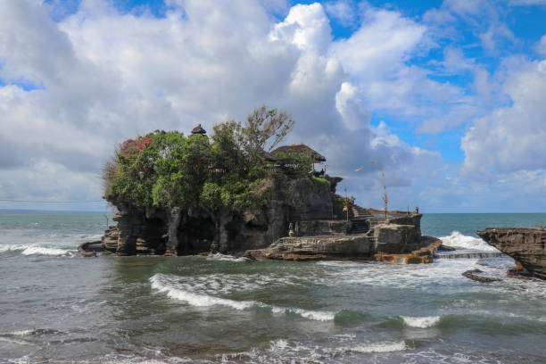 fale rozbijają się na klifie, na szczycie którego znajduje się hinduska świątynia tanah lot. świątynia zbudowana na skale w morzu u wybrzeży wyspy bali, indonezja. bujna tropikalna roślinność na szczycie klifu. - tanah lot close up bali indonesia zdjęcia i obrazy z banku zdjęć