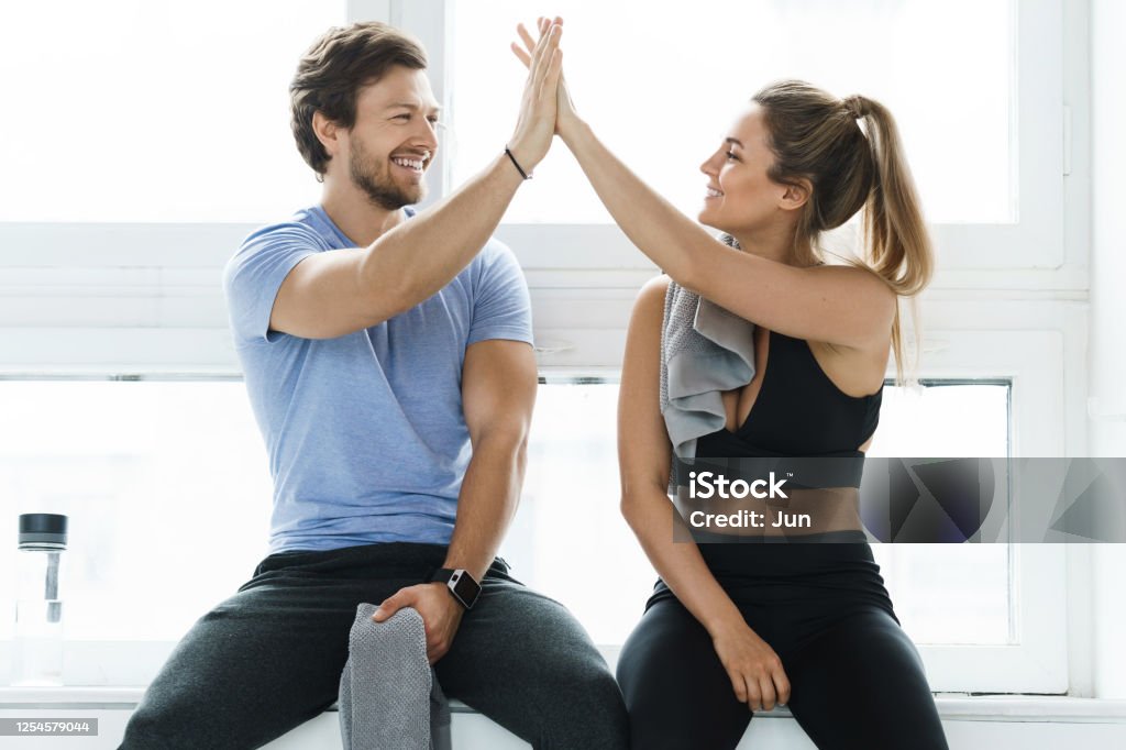 High five between man and woman in the gym after fitness workout High five between man and woman in the gym after fitness workout. Personal trainer and his client achieving results during a training. Exercising Stock Photo