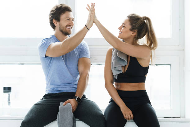 High five between man and woman in the gym after fitness workout High five between man and woman in the gym after fitness workout. Personal trainer and his client achieving results during a training. good posture photos stock pictures, royalty-free photos & images
