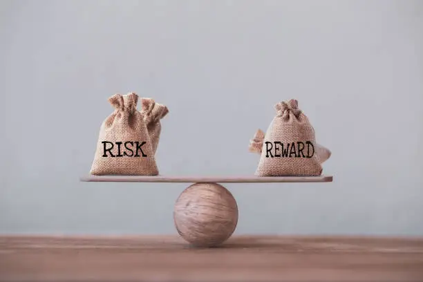 Photo of Risk and reward bags on a basic balance scale in equal position on wood table. risk management concept, depicts investors use a risk reward ratio to compare the expected return of an investment