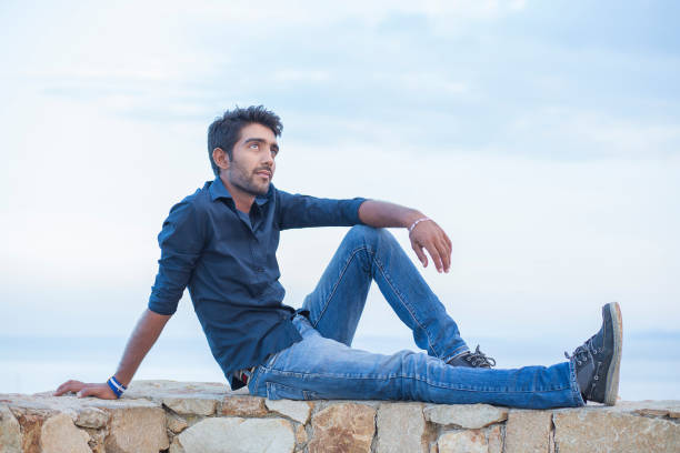 istock Man thinking looking to blue sky while sitting on a concrete bridge above the sea 1254584348