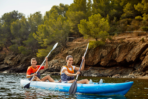 Happy man and woman kayaking on river. Smiling couple is enjoying aquatic sport during sunset. They are having fun during summer vacations.