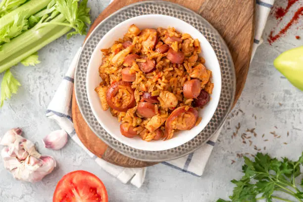 Creole jambalaya (also called "red jambalaya"). Jambalaya with chicken, sausages and vegetables in a white bowl on a concrete background top view.
