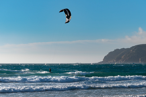 Praia do Guincho, Portugal - July 4, 2020: A kite surfer at the Guincho Beach (Praia do Guincho) near Cascais, with the Cabo da Roca on the background, in Portugal