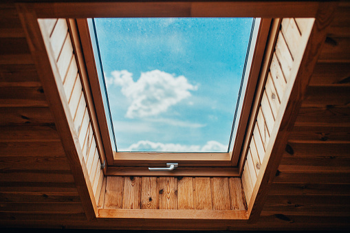 Blue bright sky with clouds through the roof window - natural light inside the house
