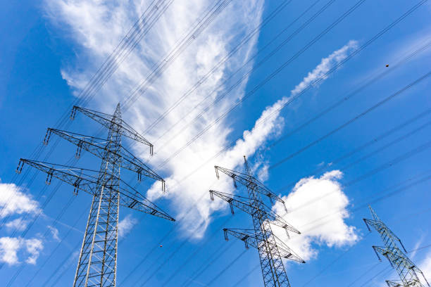Several large metal high voltage lattice crosses transporting electricity under a blue sky with white clouds
