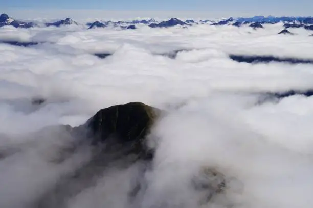 Green mountain peak surrounded by clouds - more peaks in far - Fjordland National Park - Doubtful Sound