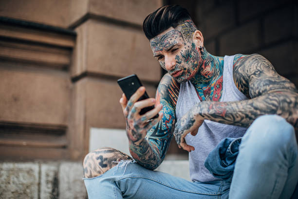 istock Modern man with whole body covered in tattoos using phone outdoors on steps 1254613170