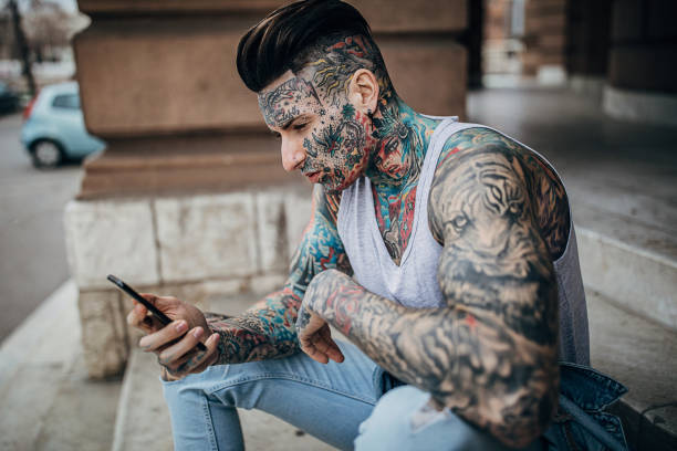istock Modern man with whole body covered in tattoos using phone outdoors on steps 1254613418