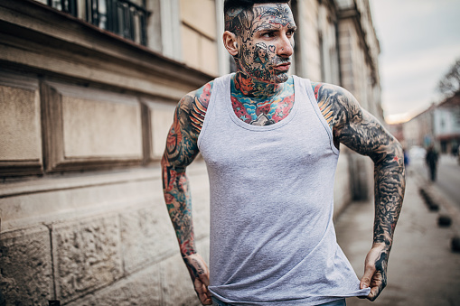One man, modern man with whole body covered in tattoos, standing on the street.