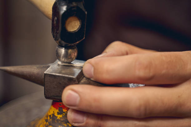 Professional Caucasian artisan using a metalsmithing tool Close up of a male hand flattening a metal part with a texturing hammer on the anvil jewelry craftsperson craft jeweller stock pictures, royalty-free photos & images