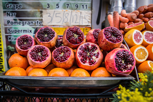 Fresh red pomegranates, oranges and carrots sold on a market place stall