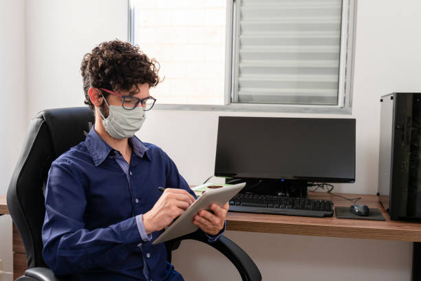 istock Businessman working in his office with protective mask, using tablet. Covid-19 Pandemic 1254641398
