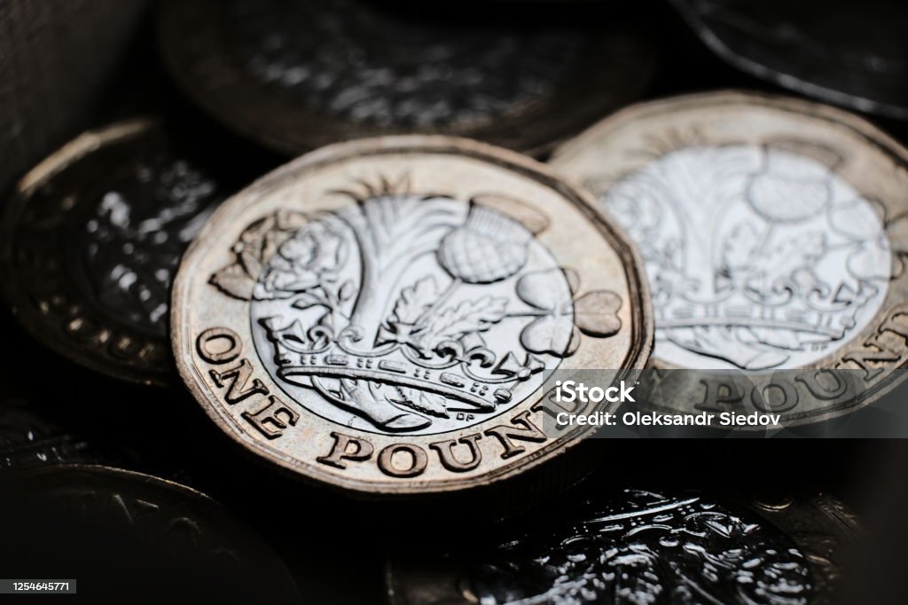 British one pound coins placed on top of each other in the box. Coins have shiny reflections and deep shadows. Macro photo with dramatic shadows. Pound Symbol Stock Photo
