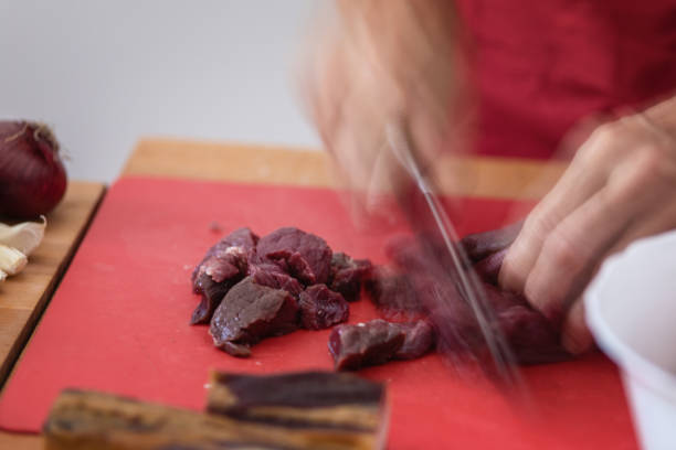 Piece of game meat cut into thin slices using sharp knife, close-up, motion blur on hand and knife