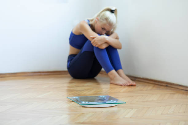 sad teenager girl with scales on floor - anorexia imagens e fotografias de stock