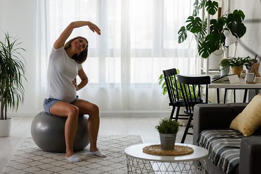 Beautiful 9 months pregnant woman exercising at home on yoga ball