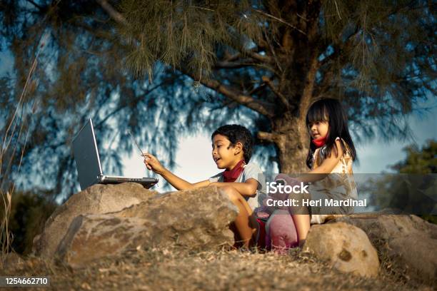 Schoolboy Study And Teach His Little Sister Using Laptops Under The Tree Stock Photo - Download Image Now