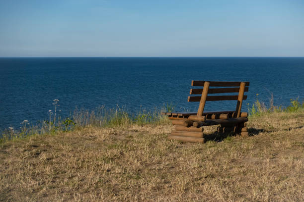 Bench on a cliff above the sea Shot on the empty wooden bench on a cliff above the sea during a sunset. sea population stock pictures, royalty-free photos & images