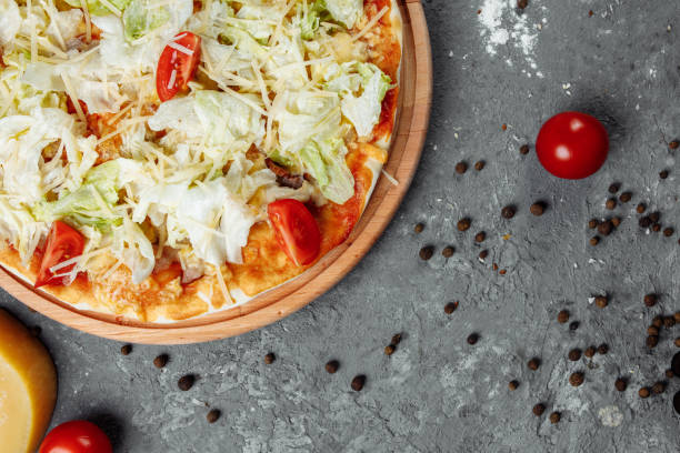 istock Delicious pizza Caesar style with white sauce, chicken, parmesan, egg, cherry tomatoes and fresh lettuce at wooden background 1254687031