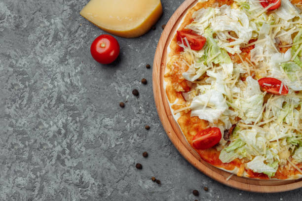 istock Delicious pizza Caesar style with white sauce, chicken, parmesan, egg, cherry tomatoes and fresh lettuce at wooden background 1254687036