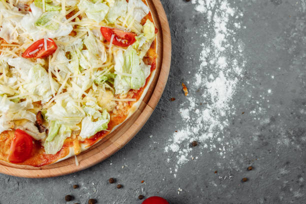 istock Delicious pizza Caesar style with white sauce, chicken, parmesan, egg, cherry tomatoes and fresh lettuce at wooden background 1254687042