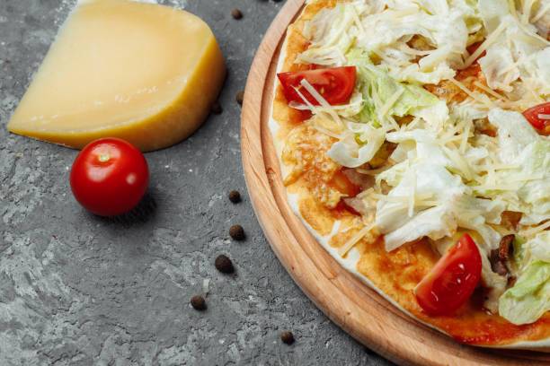 istock Delicious pizza Caesar style with white sauce, chicken, parmesan, egg, cherry tomatoes and fresh lettuce at wooden background 1254687049