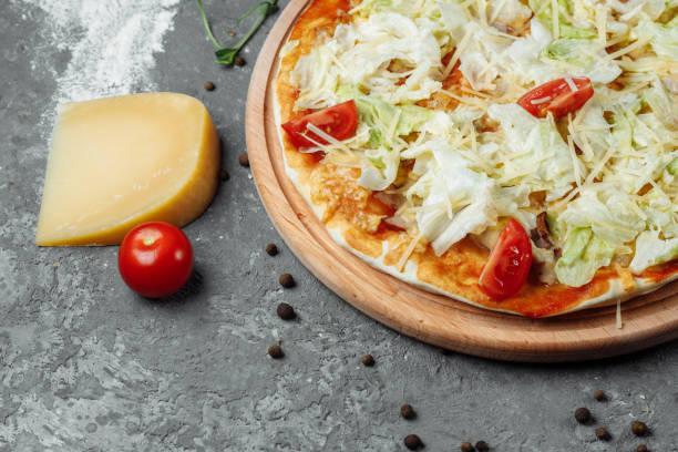 istock Delicious pizza Caesar style with white sauce, chicken, parmesan, egg, cherry tomatoes and fresh lettuce at wooden background 1254687055