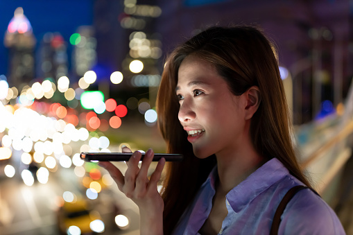 asian woman use smartphone to send voice messages outdoor at night while commuting