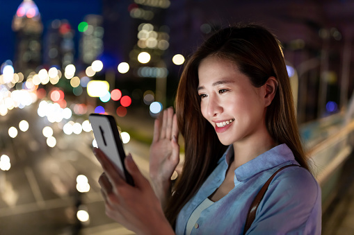 asian woman use smartphone to video chat with friends outdoor at night while commuting