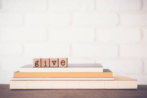 The word GIVE, letters and copy space background, vintage. The word GIVE, letters on block cubes on top of books and wooden table with white bricks background, blank copy space, vintage minimal style. Concepts of share, charity, donation and love. legacy concept stock pictures, royalty-free photos & images