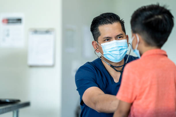 Young boy at a doctors appointment wearing a mask. Male doctor wearing a mask and gloves during a checkup with a young, 8 year old boy because of the COVID-19 outbreak. annual event stock pictures, royalty-free photos & images