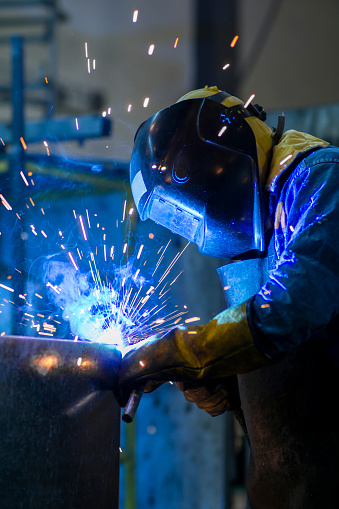 Male worker welding steel, sparks from light, protective masks and gloves increase safety