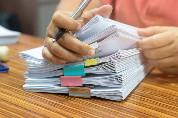 istock Teacher hand holds pen for checking student's homework assignment on table office. Paper documents stacked in archive with paperclip. Report papers stacks. Business and education concept. 1254702753