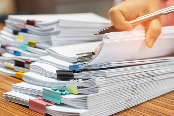 istock Teacher hand holds pen for checking student's homework assignment on table office. Paper documents stacked in archive with paperclip. Report papers stacks. Business and education concept. 1254702778