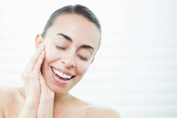 istock Young cheerful woman smiling while doing a morning routine cleansing her face 1254704029