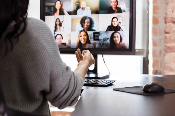 Due to COVID-19, woman video conferences from home Unrecognizable woman and colleagues video conference during the coronavirus epidemic. over the shoulder view photos stock pictures, royalty-free photos & images
