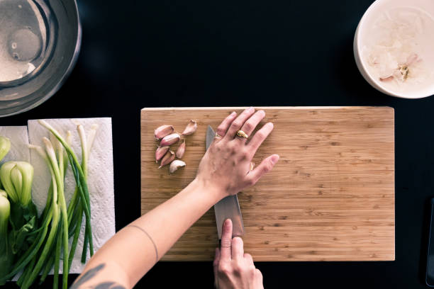 High angle view human hands crushing garlic cloves An unrecognizable woman crushes garlic with the flat side of a large knife for a recipe that includes leeks and green onions. cooking with garlic stock pictures, royalty-free photos & images