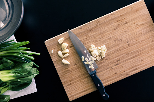 A photo of garlic partially diced on a cutting board, with other vegetables at the side.