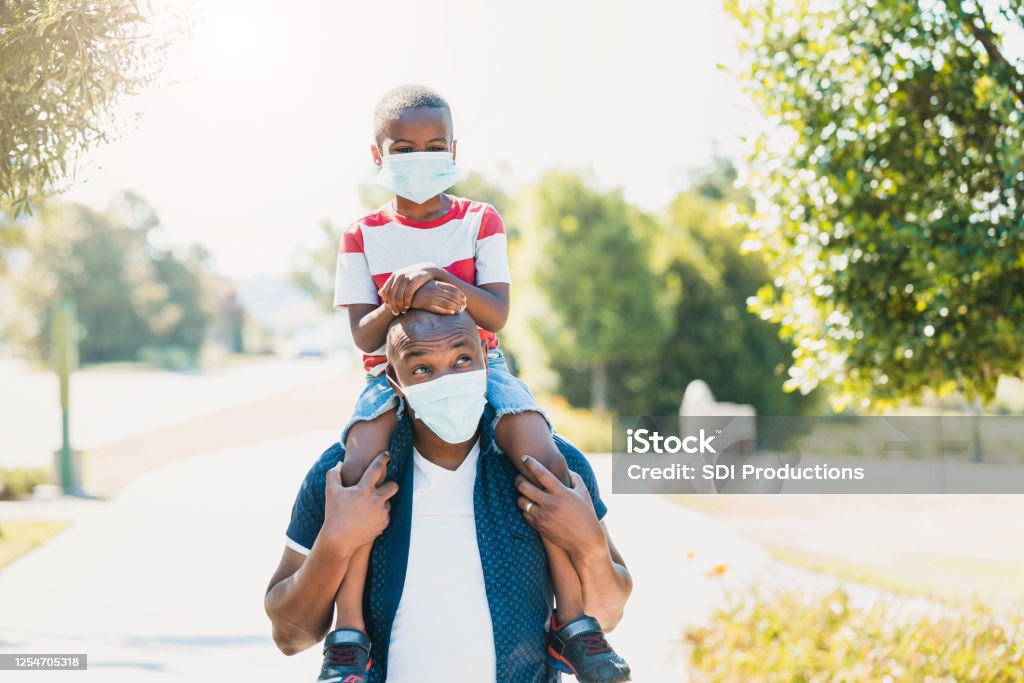 Dad gives son piggy back ride; both wear masks During COVID-19, the dad gives his young son a piggy back ride.  They are both wearing protective masks. Protective Face Mask Stock Photo
