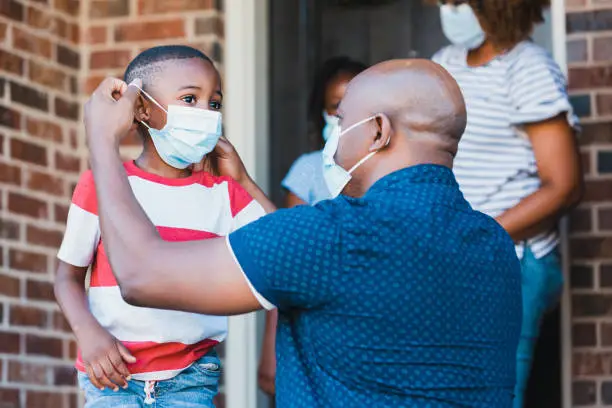 Photo of Father helps son put on protective face mask