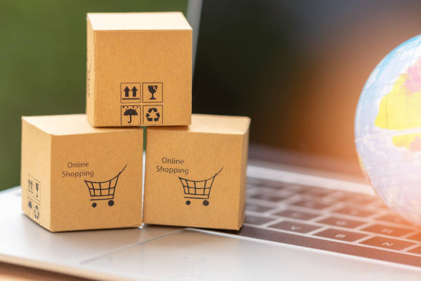istock Stack of cardboard boxes with warning and shopping cart icon on laptop keyboard with globe nearby, with nature green background. Consumer buy product anywhere. Online shopping and e-commerce concept. 1254705494