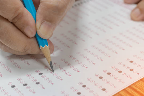 istock Dry hands of old woman is doing exams using pencil selected multiple choice on standardized test form with answers bubble. No one is too old to learn. Ideas about adult education. 1254706075