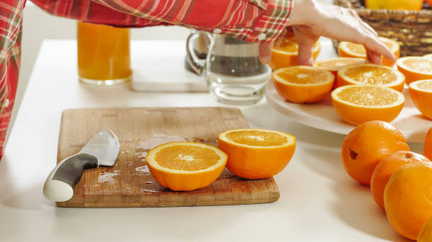 istock Woman cuts oranges on a wooden kitchen board with white background. Preparing fresh orange juice using an electric juicer. 1254710163