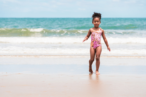 African American mixed race girl walk on the beach from beautiful blue sea. Concept of childhood, family, summer leisure and vacation