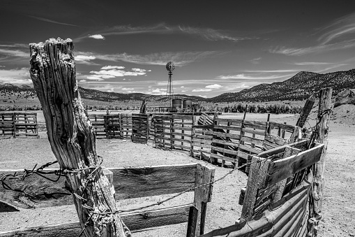 Black and White of an old western corral, windmill, and the blowing clouds.