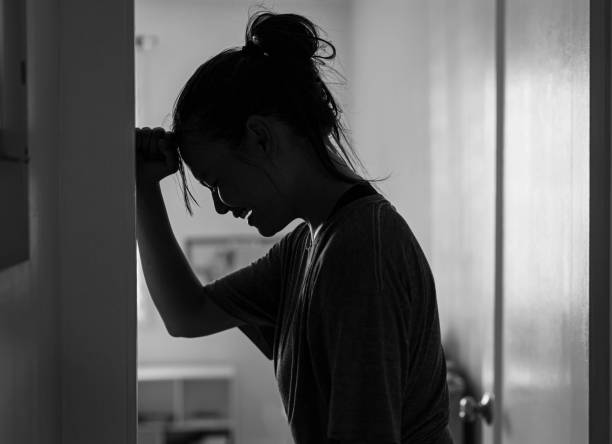 A sad woman crying and depressed in her room at home alone. A wom.an in morning and deep sorrow standing in a corner of a room at home screaming in misery woman alone dark shadow stock pictures, royalty-free photos & images