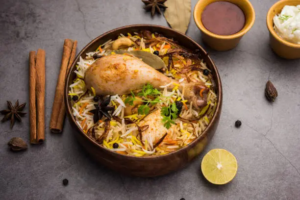 Restaurant style Spicy Chicken Biryani in wooden bowl with Raita and salan, Popular Indian or Pakistani Food