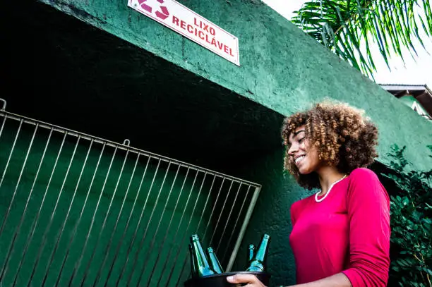 a young black woman putting bottles to recycle in a recycling holder
